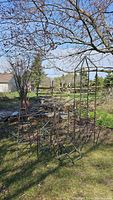 Photo showing three copper obelisks standing in a garden alongside other garden elements like a terracotta urn.