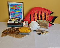 View of all items including framed print, large red metal fish, yellow fish, metal fish with cup holders, wooden plaques, and fish lures displayed on table