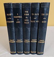 Five Hemingway novels standing upright showing spines with titles and author in gold emboss.