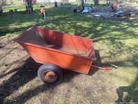Side profile of entire red metal utility trailer showing bed, wheels, hitch tongue