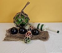 Photo showing full lot with fishing net, various glass floats, and buoy against yellow background and white table.