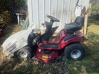 Side view of the ride-on mower showing red chassis, white detachable hood partially removed, black seat, and tires