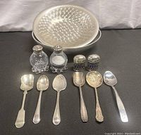 Overview of entire lot showing all sterling and silver plated salt and pepper shakers and spoons with two metal serving bowls in background.