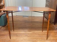 Front view of the wooden folding table showing four turned legs and wooden top.