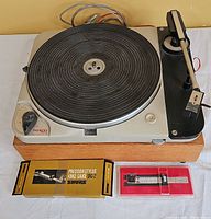 Front view of Thorens TD 124 turntable on oak base with rubber mat, tonearm, Shure gauge box and case in front.