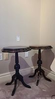 Front view of two matching mahogany accent tables against wall, showing their shape and base details.