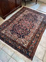 Full view of the area rug showing floral pattern and fringed edges positioned on floor next to wooden furniture.