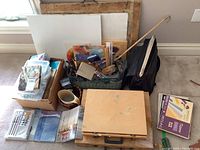 Full lot overview showing baskets of brushes, wooden art cases, boxes, and various art supplies grouped on the floor.