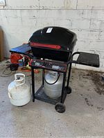 Full view of Master Chef BBQ grill on two-wheeled black metal cart with side shelves and two propane tanks, one mounted and one separate.