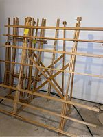 Photo shows one fully assembled wooden artist display rack with multiple horizontal bars and cross brace supports, standing on concrete floor against white wall.