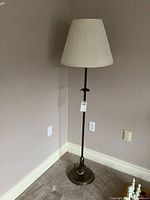 Full view of floor lamp standing in a corner with steel base and fabric shade