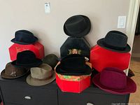 Full lot of men's and women's hats displayed on top of furniture with red hat boxes beneath and behind them.