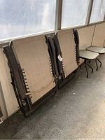 Folded brown woven mesh lounge chairs with metal frames leaned against wall indoors