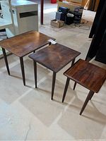 Set of three wood nesting tables positioned side by side on concrete floor with basement background.