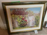 Framed oil painting on board showing a garden scene with white picket fence and red flowers, included in the frame with visible matting.