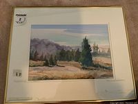 Framed watercolour landscape painting with white matte and gold frame, showing natural scenery with trees and sky.