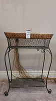 Front view of the iron plant stand showing the rattan-trimmed top basket and bottom mesh shelf with curved legs.