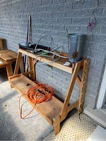 Full view of wooden potting bench with accessories on two shelves, including extension cord and metal pail.