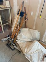 Overall group of sailboat supplies including wooden keel, ropes, sail in case, and brackets on concrete floor in basement.