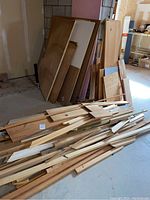 Wide view of pile showing large plywood sheets leaning against wall and many smaller trim pieces in front on floor.
