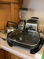 Photo shows Oster blender, Black and Decker electric skillet with glass lid, electric kettle, and 2-slice toaster on a kitchen counter.