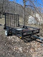 Overall view of black utility trailer parked outdoors with mesh deck and ramp gate raised