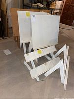 View of three wooden white tabletop easels and two wooden display shelves stacked and leaning against each other.