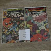 Two comic books from The Amazing Spider-Man series, issues #197 and #206, placed side by side on a wooden surface with a MaxSold lot number.