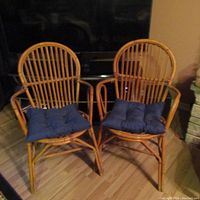 Two vintage bamboo chairs side by side with navy blue cushions on the seats. Displayed on a wood floor in front of a TV.