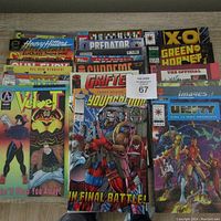 Photo of a standing stack of comic books showing colorful cover art from titles like Velvet, Predator, X-O Green Hornet, Unity and others.