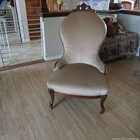 Front view of the Victorian lounge chair showing the beige upholstered seat and back with carved wooden frame and curved front legs with casters.
