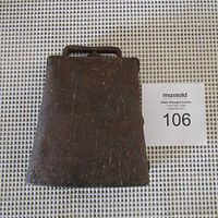 Front view of the antique cow bell showing its rusted metal surface and rectangular shape with a handle.