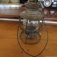 Full view of rusty antique kerosene lantern with metal frame, glass globe, vented top, and handle
