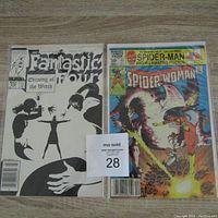 Photo of two Marvel comic books: Fantastic Four #276 and Spider-Woman #41, laid flat on a wooden surface showing front covers.