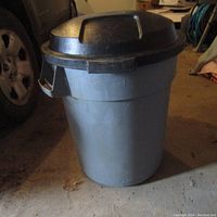 External view of Rubbermaid trash can with closed black lid, showing round gray body and side handles.