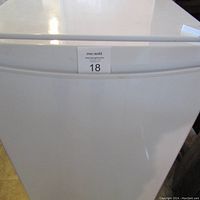 Front view of white upright freezer, door closed with handle visible
