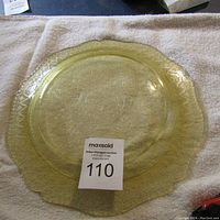 Top view of yellow depression glass platter with central embossed floral and swirl design, scalloped edges, and patterned rim.