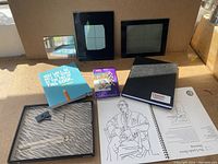 Photo showing black grid frames, boxed colored pencils, sketchbooks and art instruction book.