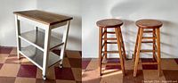 Photo showing two vintage wooden bar stools side by side and a kitchen cart with wood top and white frame on wheels.