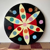 Front view of the round wooden dot art piece, showing colorful paint and varnished surface.