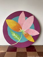 Front view of round painted floral panel with pink and yellow petals on teal and purple background.