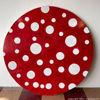 Full view of the round dot art panel against a wall showing the red base color and white dots of various sizes.