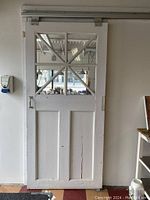 Front view of white vintage barn door on sliding rail, showing glass pane design and wooden panels below.