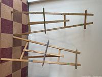 Two wooden easels standing against a wall on a checkered tile floor, showing height, structure, and condition.