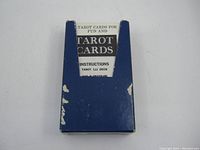 Blue cardboard box with white label containing the tarot card deck, showing wear and damage