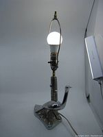 Front view of the lamp illuminated showing the working light bulb and overall bird shape design with chrome metal finish.