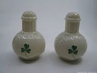 Front view of two cream-colored ceramic Belleek salt and pepper shakers with shamrock and seashell designs.