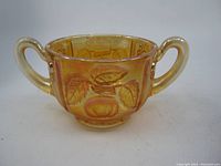 Front and side view of the marigold carnival glass apple panel open sugar bowl showing embossed apple and leaf design with two handles.