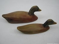 Top angled view of two hand carved wooden duck decoys showing overall shape, colors and condition including repaired head on larger decoy.