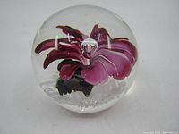 Clear glass paperweight with purple flower design inside, viewed from a slight angle showing the flower details.